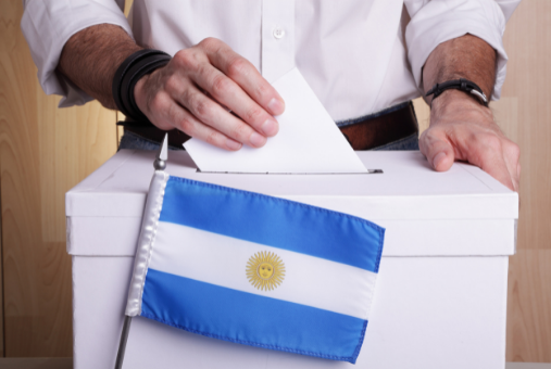Person putting a card in a ballot box in front of the flag of Argentina