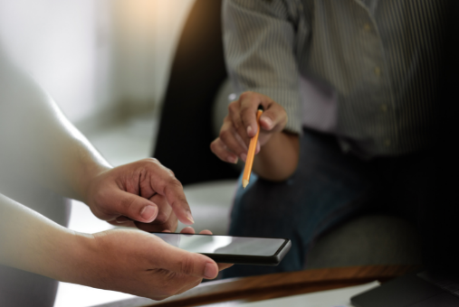 A person holding a phone and another pointing a pencil at it