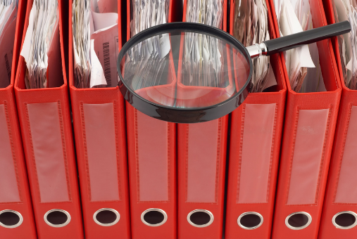 Binders of papers with a magnifying glass laying on top