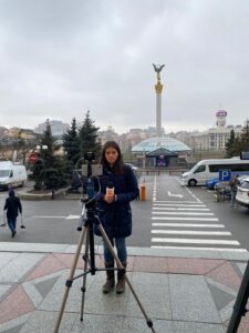 woman standing in front of monument with a camera and wearing a jacket in Ukraine