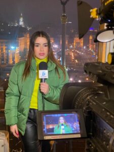woman in green puffy jacket with microphone speaking in Ukraine