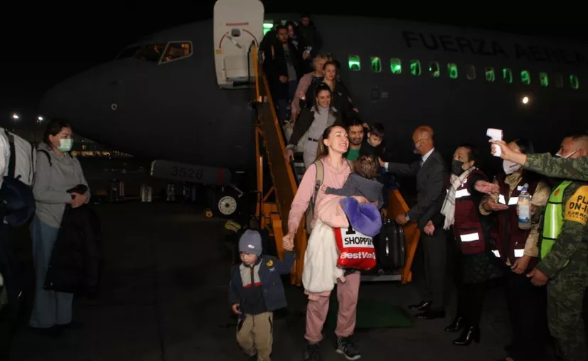 Woman carrying a baby and holding a child's hand at the bottom of the airplane stairway greets reporters.