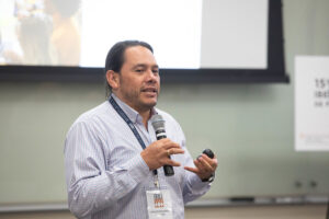 Carlos Eduardo Huertas, standing and holding a microphone during a presentation