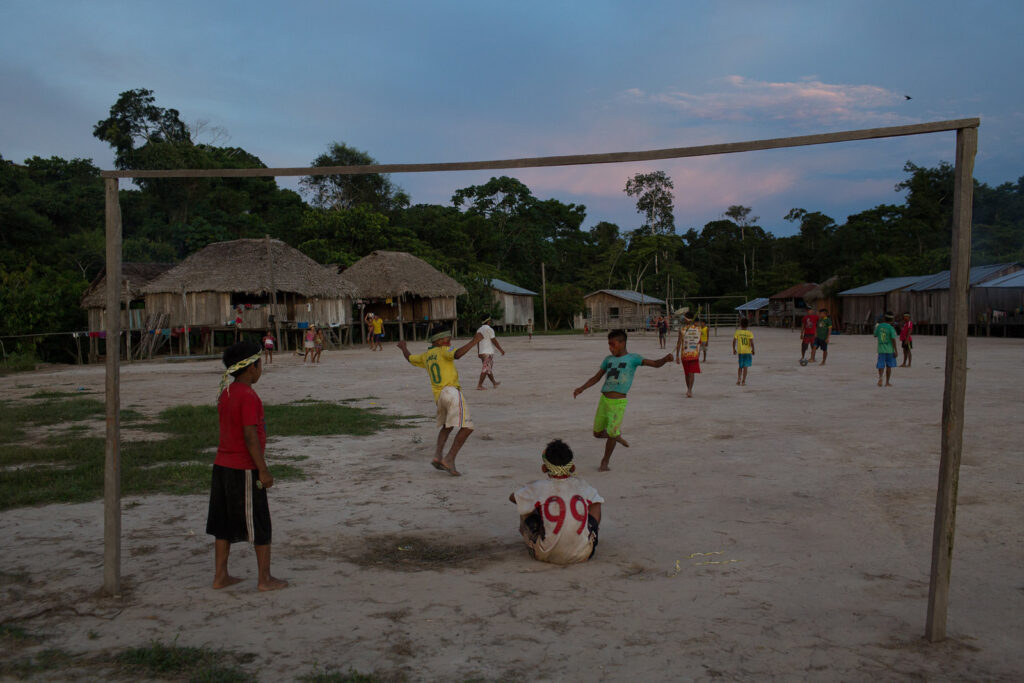 Niños indígenas juegan fútbol en un campo en el centro de su villa.