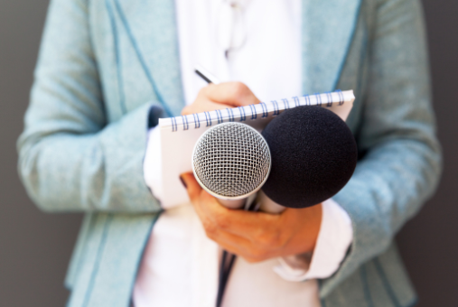 a woman holding a microphone, a notebook and a pen