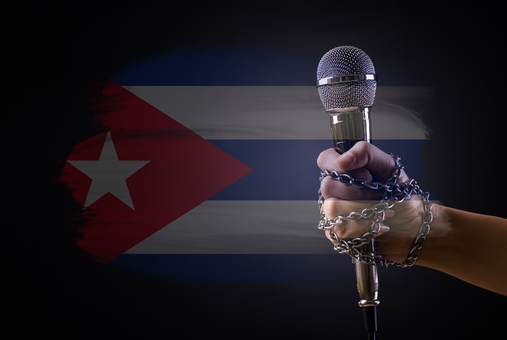 a chained hand holding a microphone. In the background the Cuban flag.