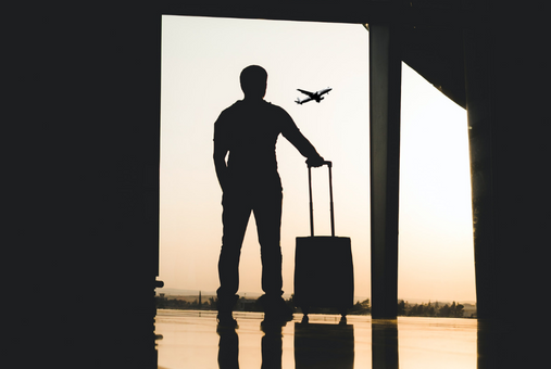 person standing at an airport and staring at an airplane in the sky