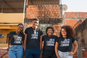 Um grupo de quatro jovens afro-brasileiros com camisetas pretas em frente a uma parede de tijolos em Jacarezinho, uma favela no Rio de Janeiro, Brasil