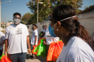 Pessoas usando máscaras e carregando sacolas plásticas vermelhas e laranjas no Brasil