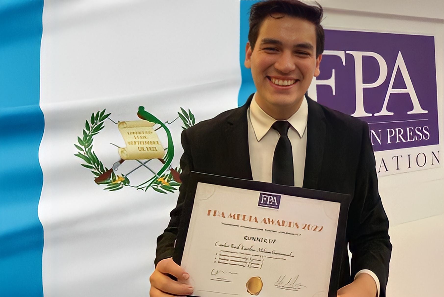 Guatemalan journalist Carlos Kestler accepting an award by the Foreign Press Association of London with a Guatemalan flag as background