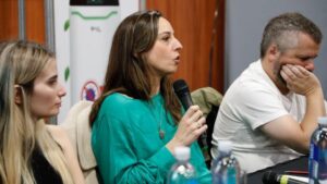 A woman with long brown hair and a bright green shirt takes the microphone and speaks at a panel in Argentina.