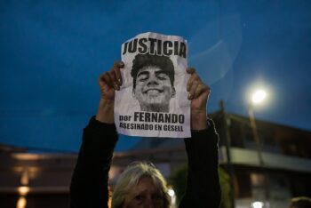 Woman at night holding a poster with the face of Fernando Baez calling for justice.
