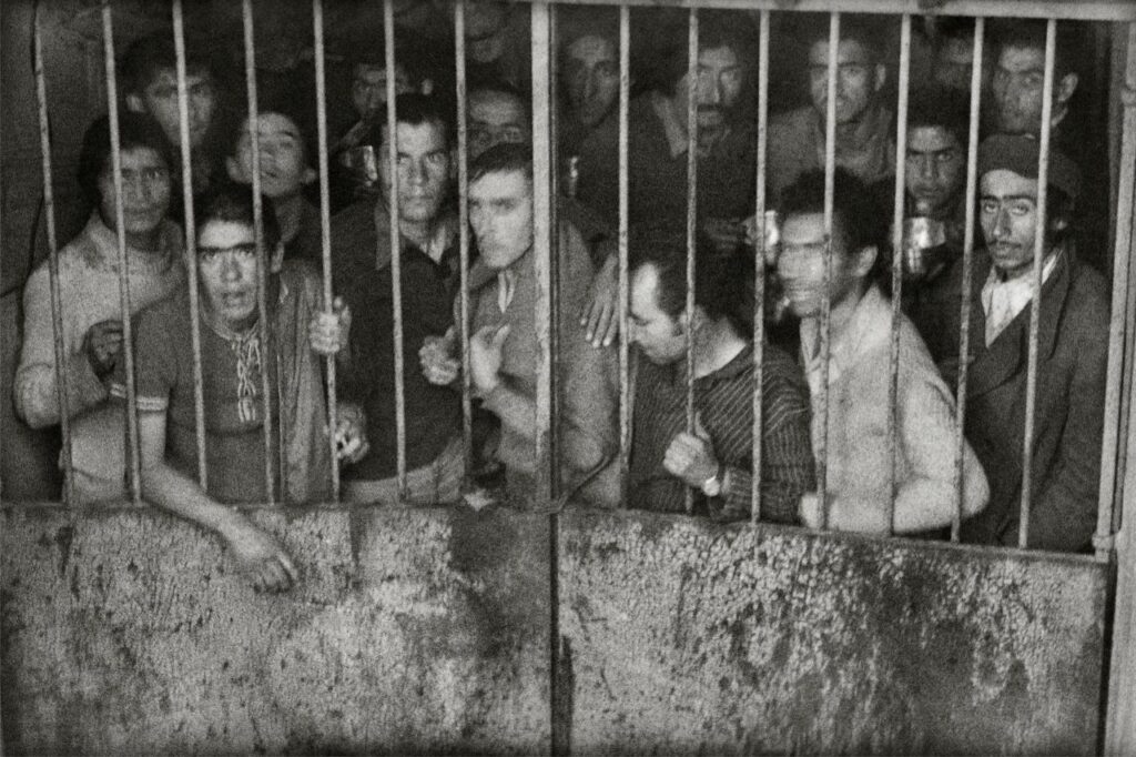 Al menos 20 hombres de pie cerca de la reja de una celda mirando a la cámara