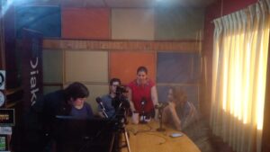 Mesa con cuatro personas sentadas con micrófonos al frente en una estación de radio.
