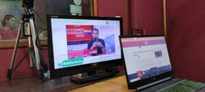 Dos computadores portátiles abiertos en noticias sobre las elecciones de Paraguay, en el fondo se ve una mujer en una estación de radio