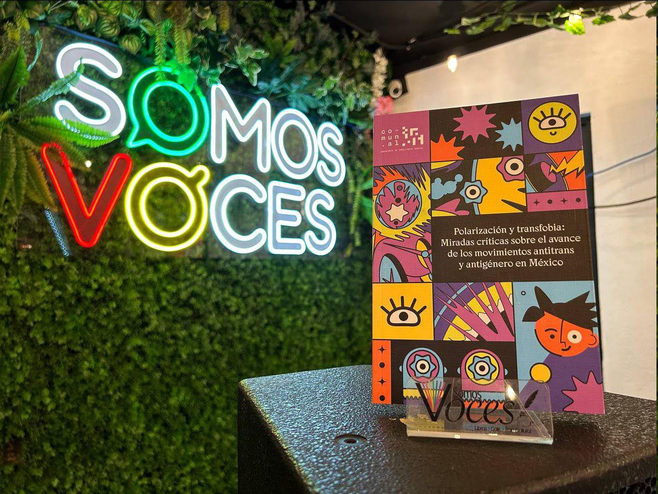 Neon sign that reads "Somos Voces" and a book on the right with bright colors on the cover
