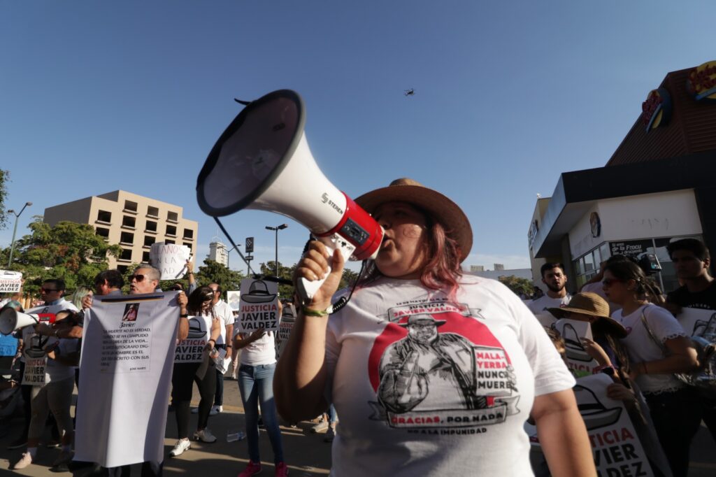 Mujer en medio de una protesta hablando a través de un megáfono con una camiseta con la imagen del periodista Javier Valdez