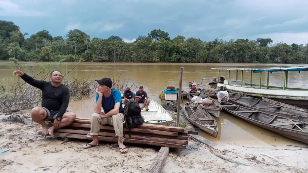 two men sitting in a bank of a river talking