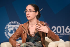 a woman with glasses on a stage in a conference