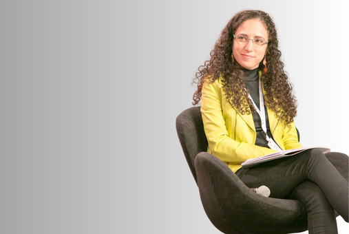 A woman with curly hair sitting in a chair on a stage.