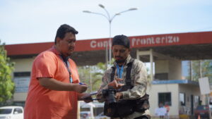 Two men at a border crossing in South America looking at a camera with a big lens and writing something in a notebook