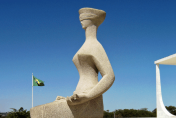 A stone statue of a blindfolded woman representing Justice in front of a building and the clear sky in Brasilia