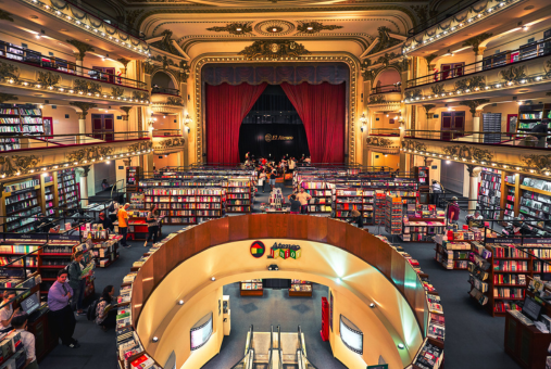 A panoramic view of a  splendid bookstore, with several floors; in the back, the curtains of a cinema theater