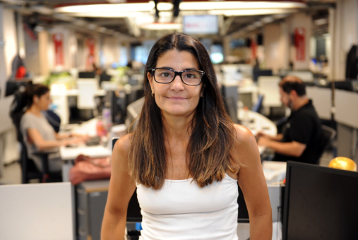 woman in a newsroom with a white top looking at the camera