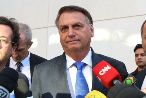 Former Brazilian president Jair Bolsonaro, wearing a suit and a blue tie, in front of microphones from journalists