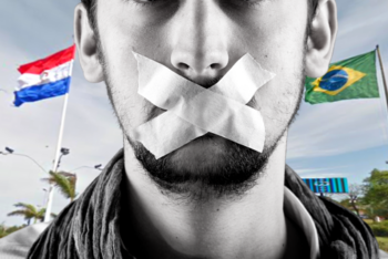 man with some tape on his mouth cannot speak, with the flags of Brazil and Paraguay in the background