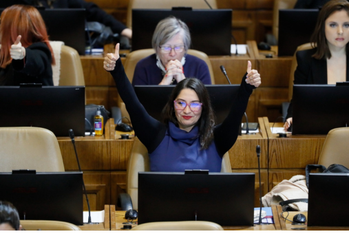Woman in dark blue dress with black sleeves give a double thumbs up at the Chilean deputies chamber.