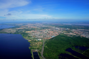 An aerial view of Ciudad Guayana in the Venezuelan Amazon. The Caroní River can be seen on the left, while the town occupies the central portion. In the distant right, the Orinoco River flows, and in the foreground to the right, there's a lush forest