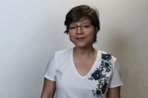 Woman with short hair and glasses looks at the camera. 