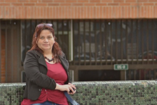 Mujer de pie apoyando su cuerpo sobre un muro sonriendo a la cámara