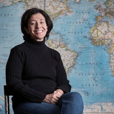 white woman sitting on a chair and smiling in front of a world map wallpaper