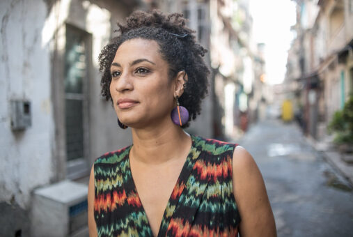 A portrait of the late councilwoman Marielle Franco in the Maré favela in 2018. She's wearing a black dress with details in green and red