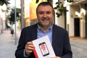 ): Ismael Nafría, Spanish author, journalist, and consultant, holding a copy of his new book "Clarín, updated' wearing a blazer on the street