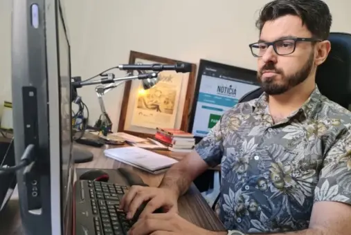Homem sentado em frente a computador com mãos sobre teclado