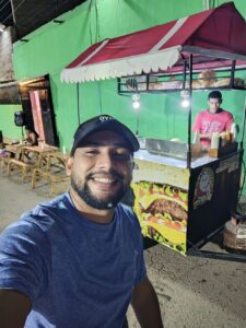 a person smiling in front of a hot dog cart