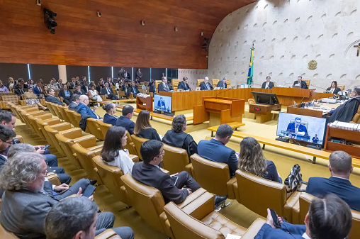 Uma foto da Sala do Supremo Tribunal Federal no Brasil, com juízes sentados ao fundo e pessoas observando um julgamento.