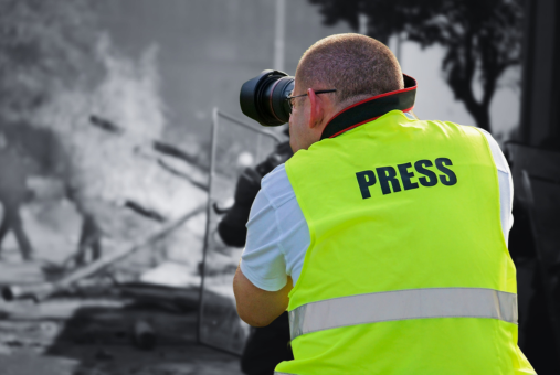 A photographer wearing a press vest photographs a protest.