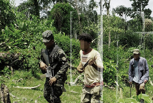 Men dressed in military clothing and armed march in a line through the jungle