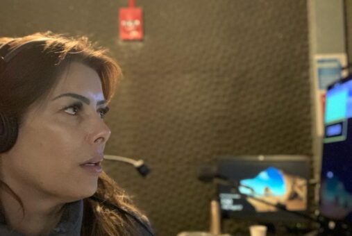 A woman wearing a white blouse and headphones looking at a screen inside a studio