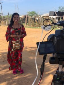 Periodista joven parada frente a una cámara sosteniendo un micrófono vestida de manera tradicional indígena Wayúu