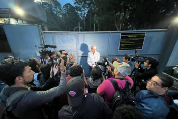 A man in a white shirt stands outside of a prison gate while journalists wait for a statement