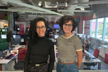 two women standing in a newsroom and smiling at the camera