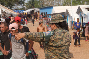 Soldier directing people on a street lined with buildings and tents