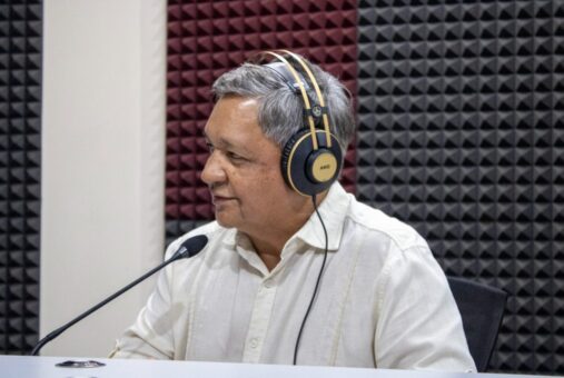 A man, Oscar Pérez, regional coordinator of AMARC for Latin America, is sitting inside a radio studio in front of a microphone. He is focused, with studio equipment visible around him.