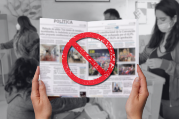 A pair of hands hold an open newspaper with a large red “no” symbol over it, suggesting misinformation or distrust in news sources. In the blurred background, people wearing masks participate in a voting process.