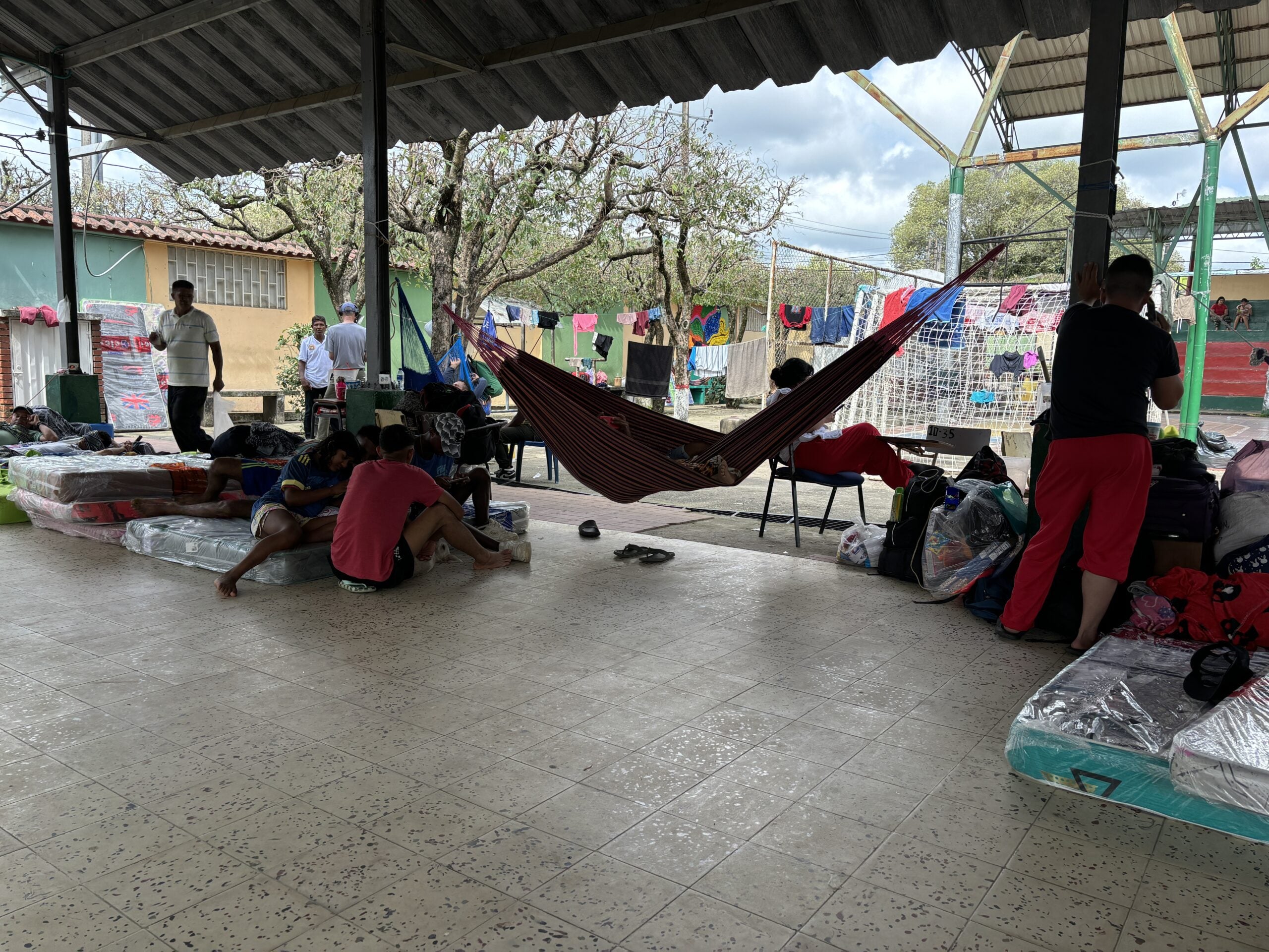 Personas desplazadas de Colombia ubicadas en un patio de un colegio. Se ven colchones en el piso, maletas y ropa colgada